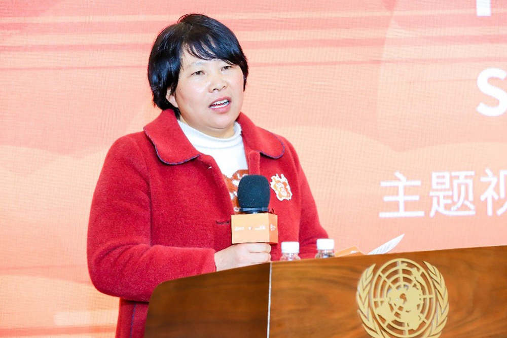 A woman standing at a lectern with a microphone addressing an audience.