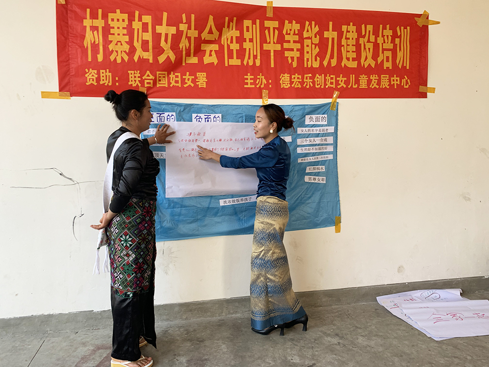 Two women stand together reading a sign on a wall